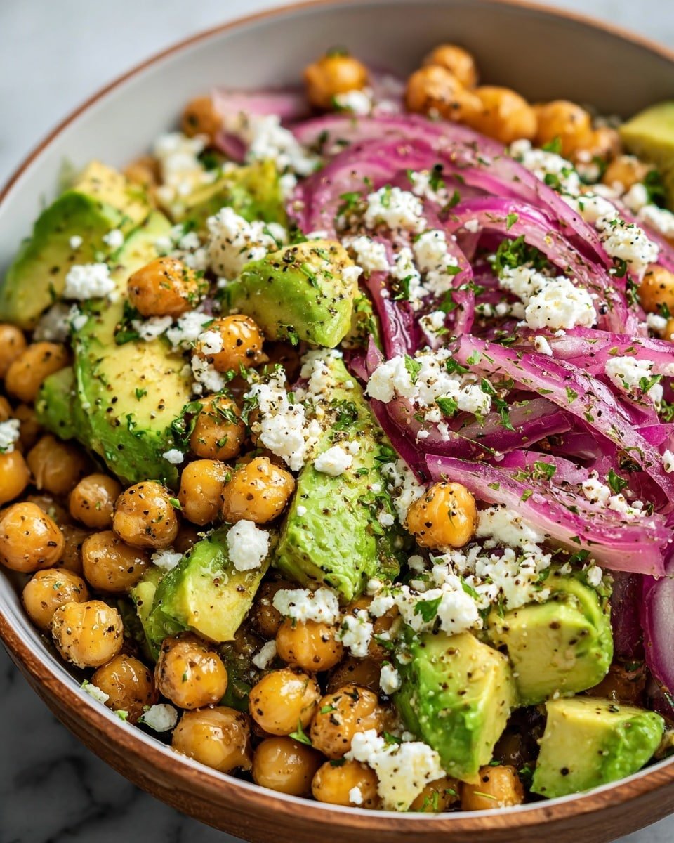 A close-up view of a salad in a white bowl with a wooden rim, placed on a white marbled surface. The salad has three main layers: the first layer is light golden chickpeas scattered all over; the second layer features chunks of bright green avocado with a creamy texture; the third layer includes thin slices of purple-red onion. Crumbled white cheese is sprinkled evenly on top, along with chopped green herbs and cracked black pepper, giving the salad a fresh and colorful look. Photo taken with an iphone --ar 4:5 --v 7